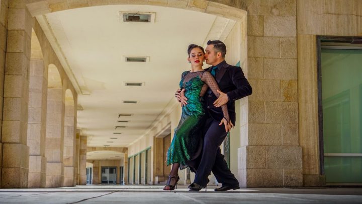 Pareja bailando tango en una milonga con músicos y público en un salón porteño.